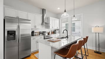 Cocina moderna con electrodomésticos de acero inoxidable, armarios blancos, una isla de mármol y taburetes de bar.