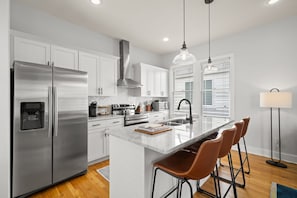 A modern kitchen with stainless steel appliances, white cabinetry, a marble island, and bar stools.