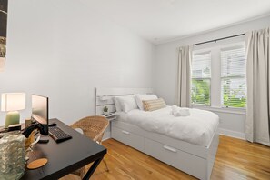 Ein Schlafzimmer mit Bett, Schreibtisch, Stuhl, Lampe und einem Fenster mit Vorhängen.