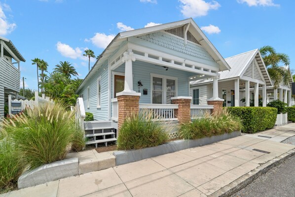 A coastal house with a porch, white railings, and a brick foundation.