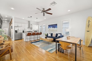 A modern kitchen with white cabinets, a stainless steel refrigerator, and a dining area with a wooden table and chairs.