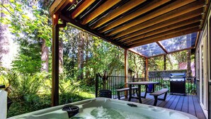 Un jacuzzi con cubierta de madera, rodeado de abundante vegetación y altos árboles.