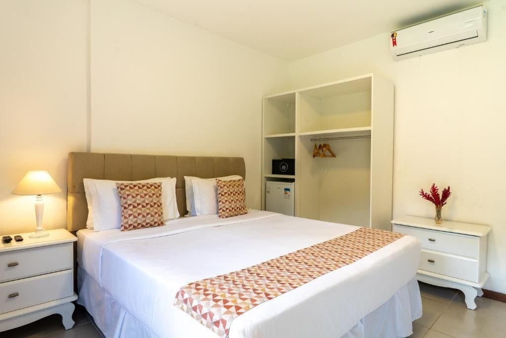 Un dormitorio ordenado con cama, mesitas de noche, un armario y un aire acondicionado.