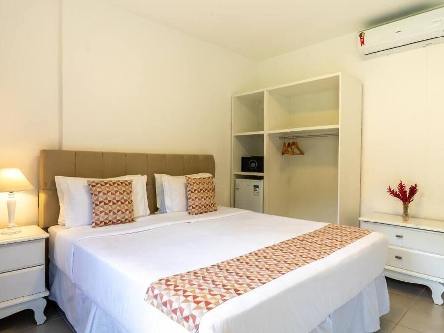 Un dormitorio ordenado con cama, mesitas de noche, un armario y un aire acondicionado.
