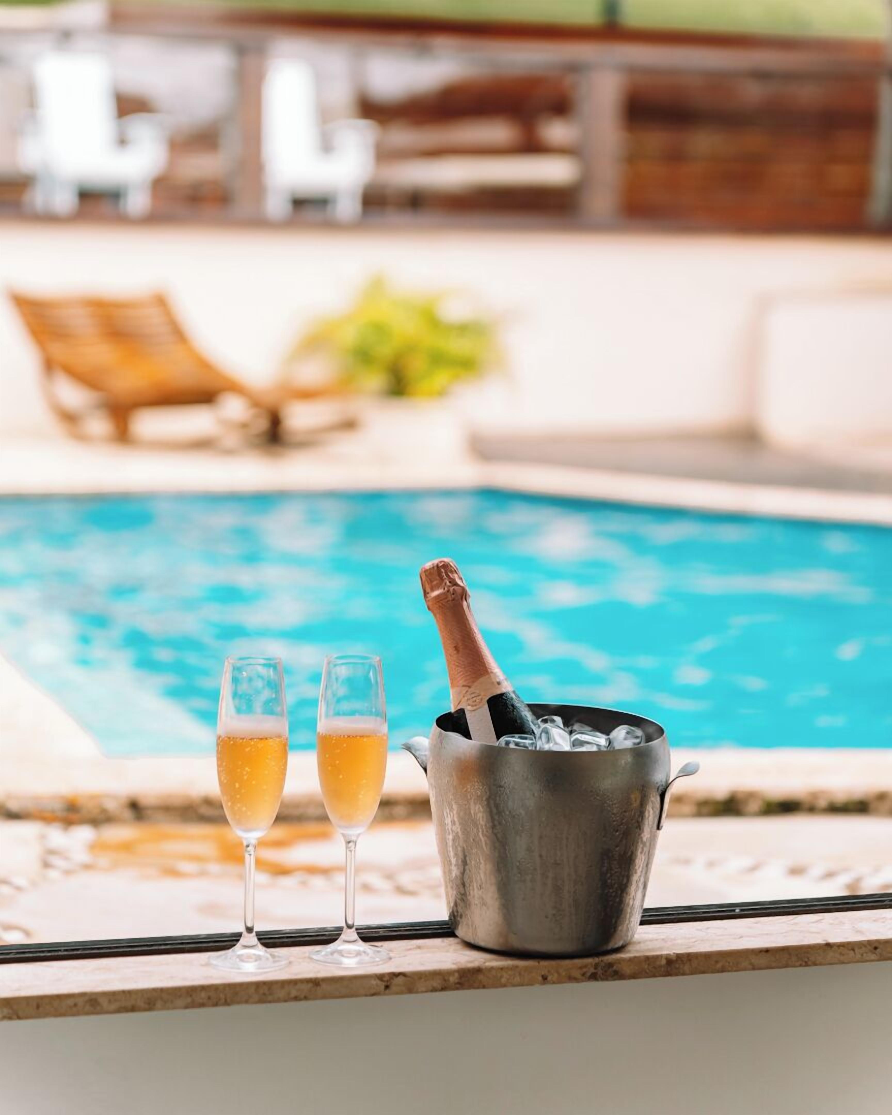 Et poolmiljø med to glas champagne og en flaske i en spand.
