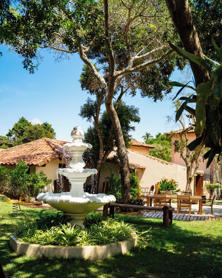 A garden with a central fountain, surrounded by greenery and a patio area with outdoor furniture.