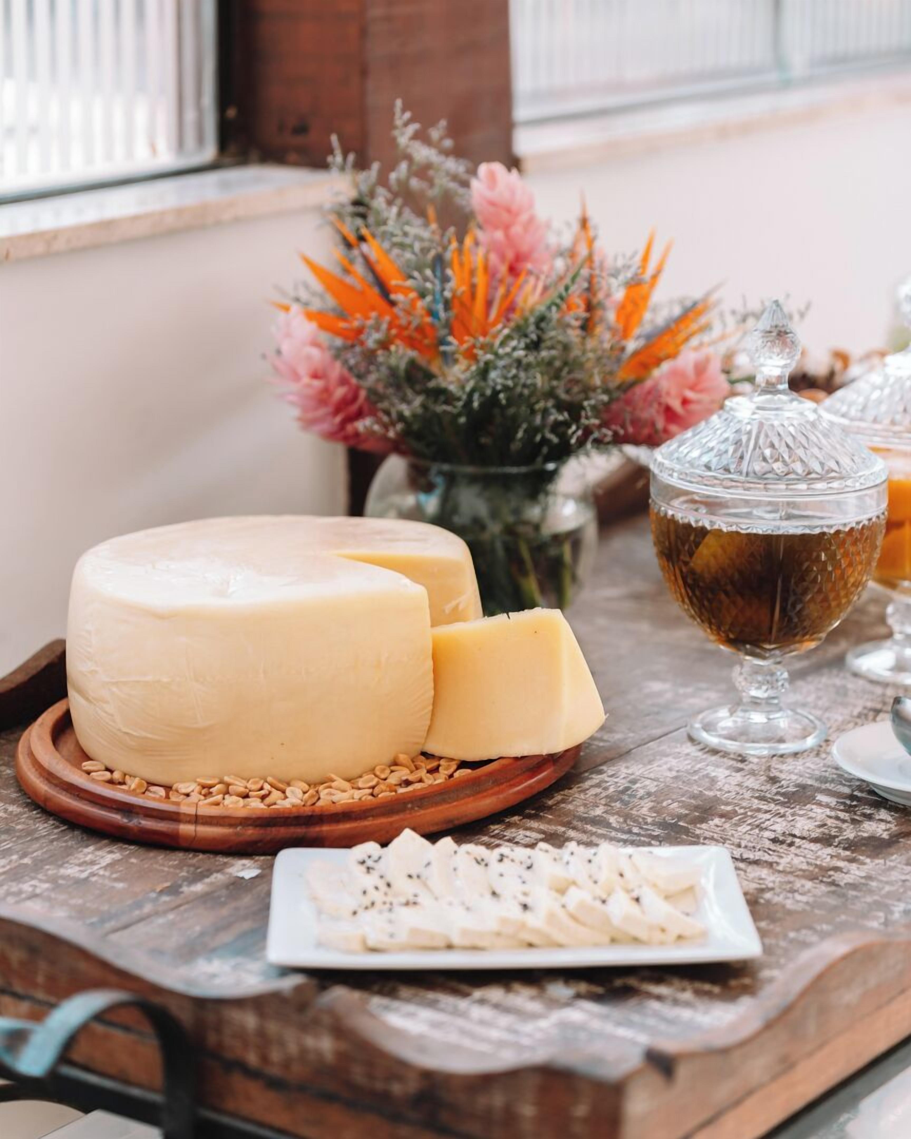 Una tabla de quesos con una rueda grande de queso, porciones más pequeñas y un recipiente de vidrio con miel, todo sobre una mesa de madera.