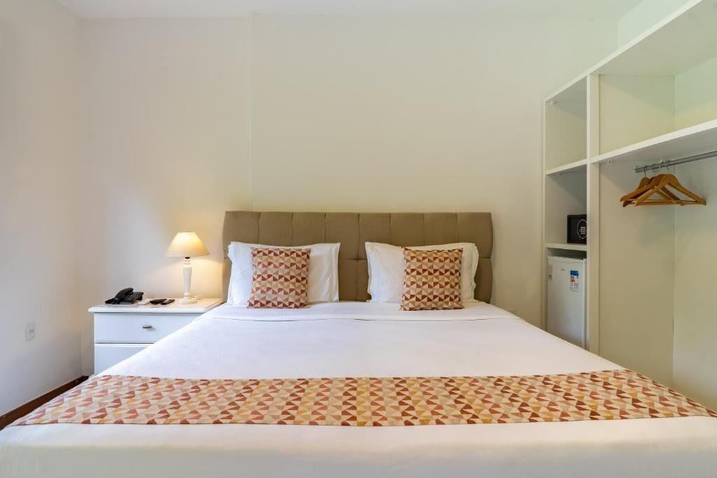 Un lit bien fait, recouvert d’une couvre-lit à motifs, une lampe de chevet et une table de chevet sur laquelle se trouvent un téléphone et une petite boîte.