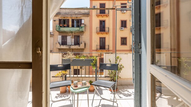 Een balkon met twee stoelen en een kleine tafel, met uitzicht op een rij kleurrijke gebouwen.