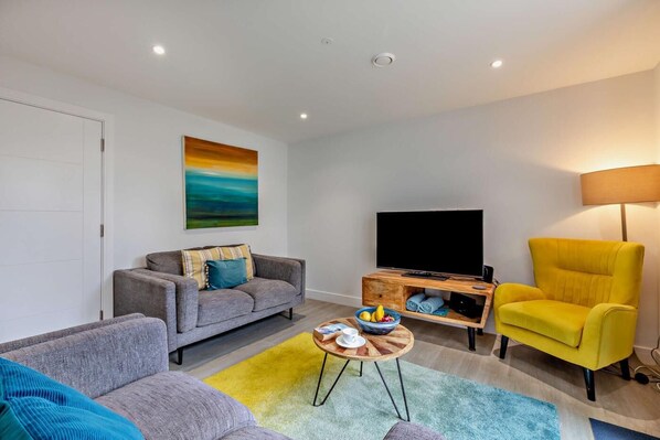A modern living room with a grey sofa, a yellow armchair, a flat-screen TV, and a painting on the wall.