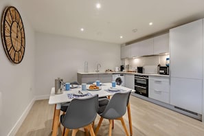 A modern kitchen with white cabinets, a built-in oven, and a dining area with a table set for two.