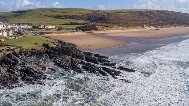 Un paysage côtier comprenant une plage, une côte rocheuse et une ville avec des bâtiments.