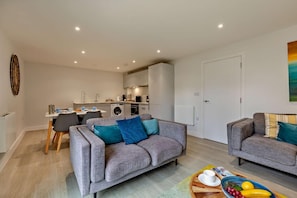 A modern apartment with a dining area, kitchen, and two sofas.
