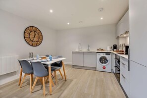 A modern kitchen with a built-in washing machine, a dining area with a table and chairs, and a large wall clock.