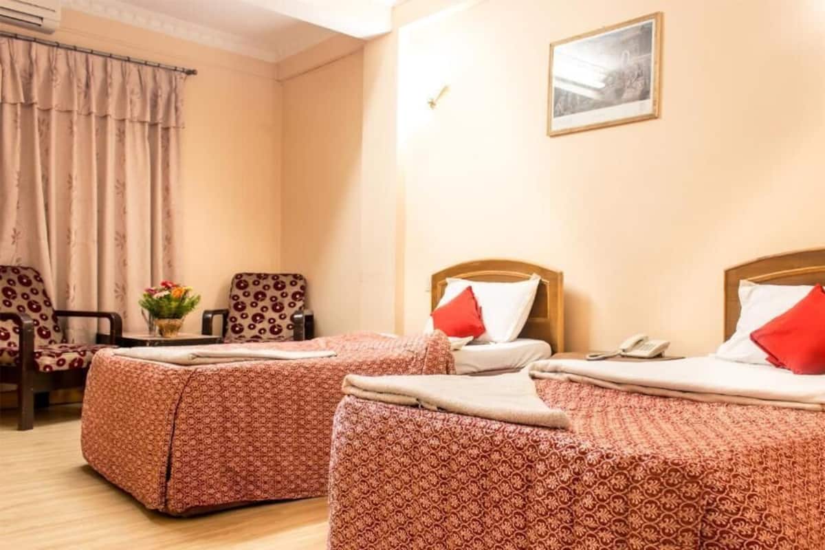 Et hotelværelse med to senge, et lille bord med en blomstervase og en stol.