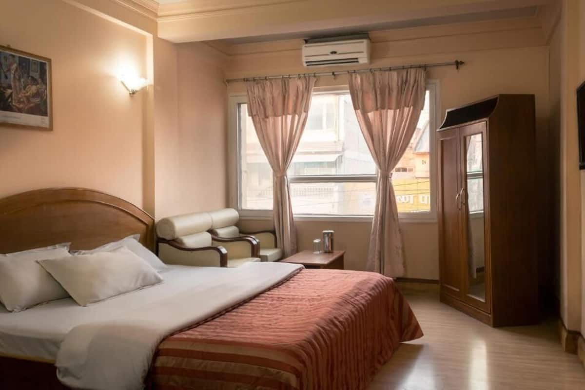 Et hotelværelse med seng, siddeområde med stol og bord, et garderobeskab og et vindue med gardiner.