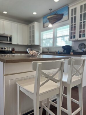 A kitchen with white cabinets, a wooden countertop, and two white bar stools. - Oak trees, Heated Pool oasis & walk to beach! Drive to downtown 3 min! (Gulfport)