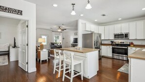 A modern kitchen with white cabinetry, stainless steel appliances, and a central island with bar stools. - Oak trees, Heated Pool oasis & walk to beach! Drive to downtown 3 min! (Gulfport)