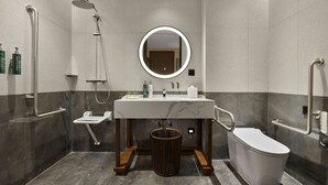 A modern bathroom with a shower, toilet, and sink, equipped with grab bars and a round mirror.