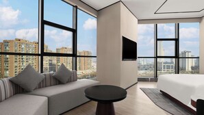 Une chambre d’hôtel moderne dotée de grandes fenêtres, d’un canapé, d’une table ronde et d’un lit.