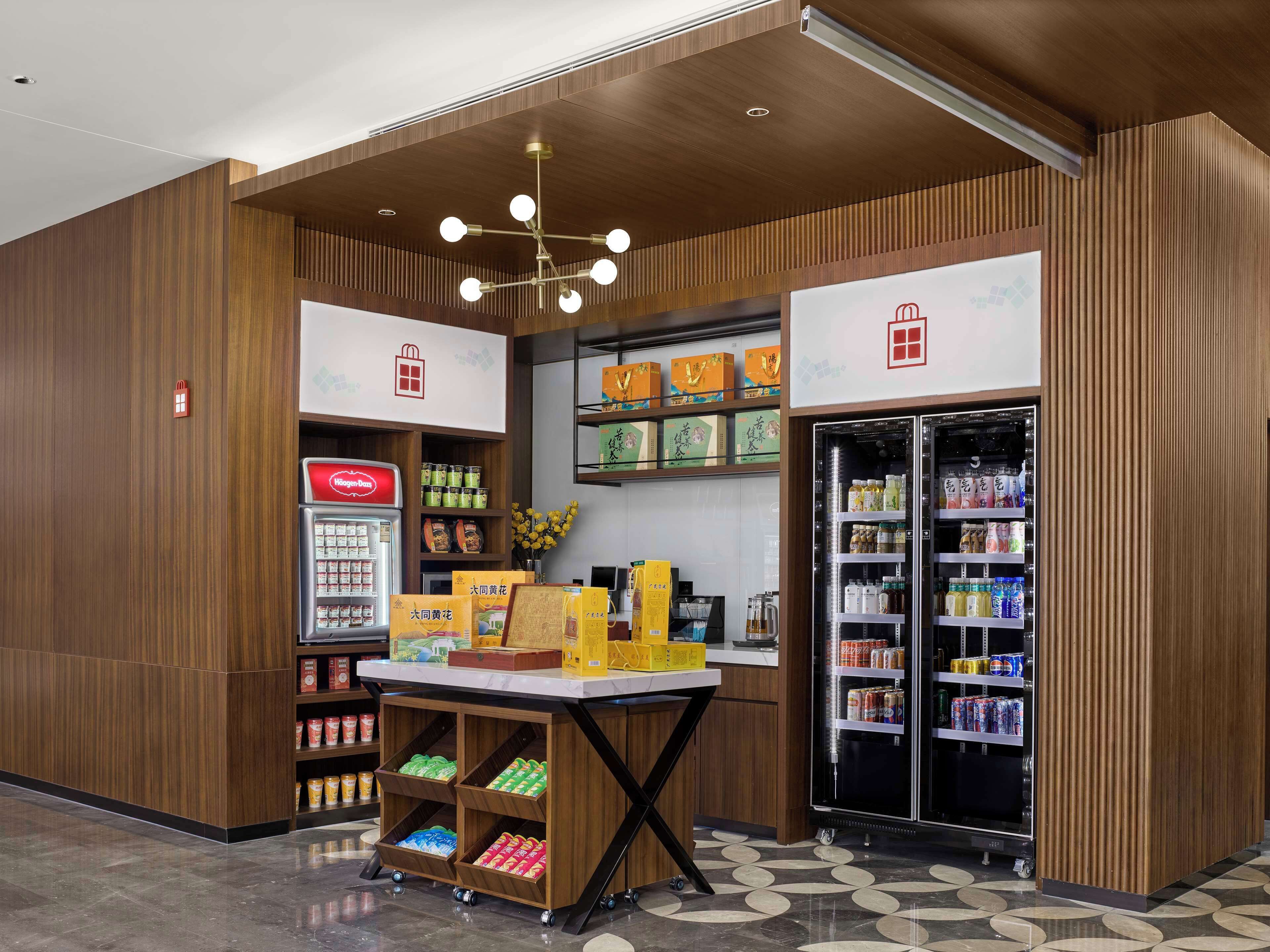 Un espacio comercial moderno con paneles de madera, una mesa expositora central y estantes refrigerados llenos de bebidas.
