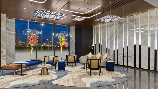 Un hall d’hôtel moderne doté d’un espace salon, de grandes fenêtres et d’un éclairage contemporain.