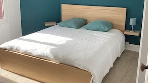 A bedroom with a wooden bed frame, teal walls, and a white bedspread.