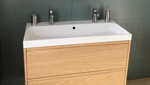 A bathroom with a white sink, two faucets, and a wooden vanity with drawers.