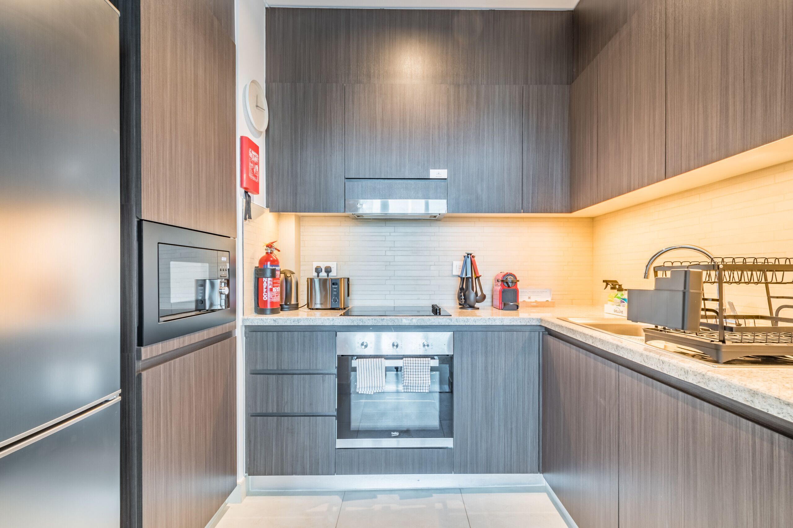 A modern kitchen with dark wood cabinets, a built-in oven, a microwave, and a coffee machine.
