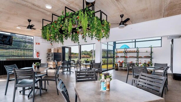 A modern restaurant with a high ceiling, hanging plants, and a view of the outdoors.