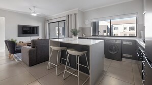A modern kitchen with a central island, bar stools, a washing machine, and a flat-screen TV mounted on the wall.