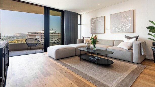 A modern living room with a sectional sofa, a coffee table, and a view of the city through large windows.