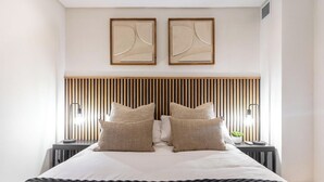 A modern hotel room with a large bed, two bedside tables, and a headboard with vertical slats.
