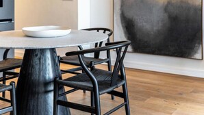 A modern dining area with a round table, black chairs, a hanging pendant light, and a large abstract painting on the wall.