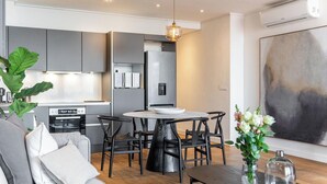 A modern kitchen with grey cabinets, a stainless steel refrigerator, and a dining area with a round table and chairs.