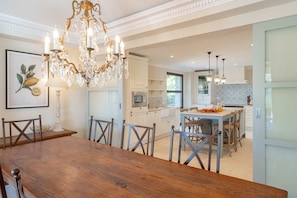 A spacious kitchen with white cabinetry, a wooden dining table, and a chandelier.