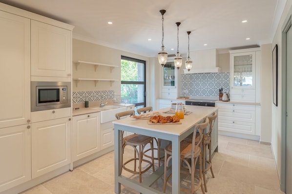 A modern kitchen with white cabinetry, a built-in microwave, a dining table with chairs, and pendant lights.