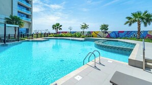 A swimming pool with a tiled deck, surrounded by palm trees and a colorful mural. - Luxury Skyline Studio | Pool and Stunning Views (Dubai)