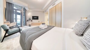A modern hotel room with a large bed, a desk, and a TV. - Luxury Skyline Studio | Pool and Stunning Views (Dubai)
