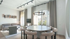 A modern living room with a round dining table, grey sofas, and a chandelier. - Sweett | The Diagonal Suites III (Barcelona)