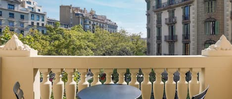 Un balcón con una mesa redonda y dos sillas, con vistas a un paisaje urbano con edificios históricos y árboles.