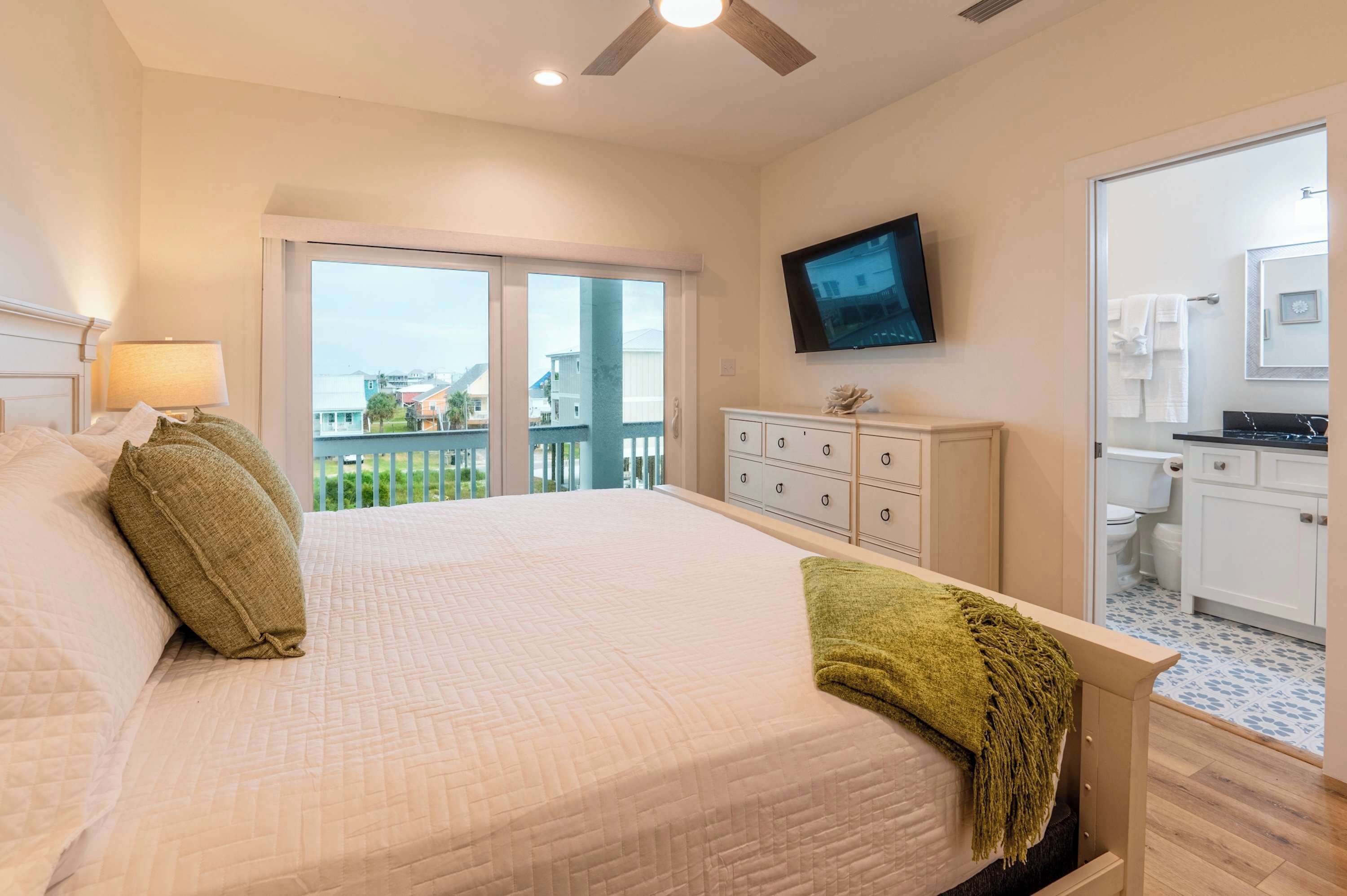 A hotel room with a large bed, a television, a balcony with a view, and a kitchenette.