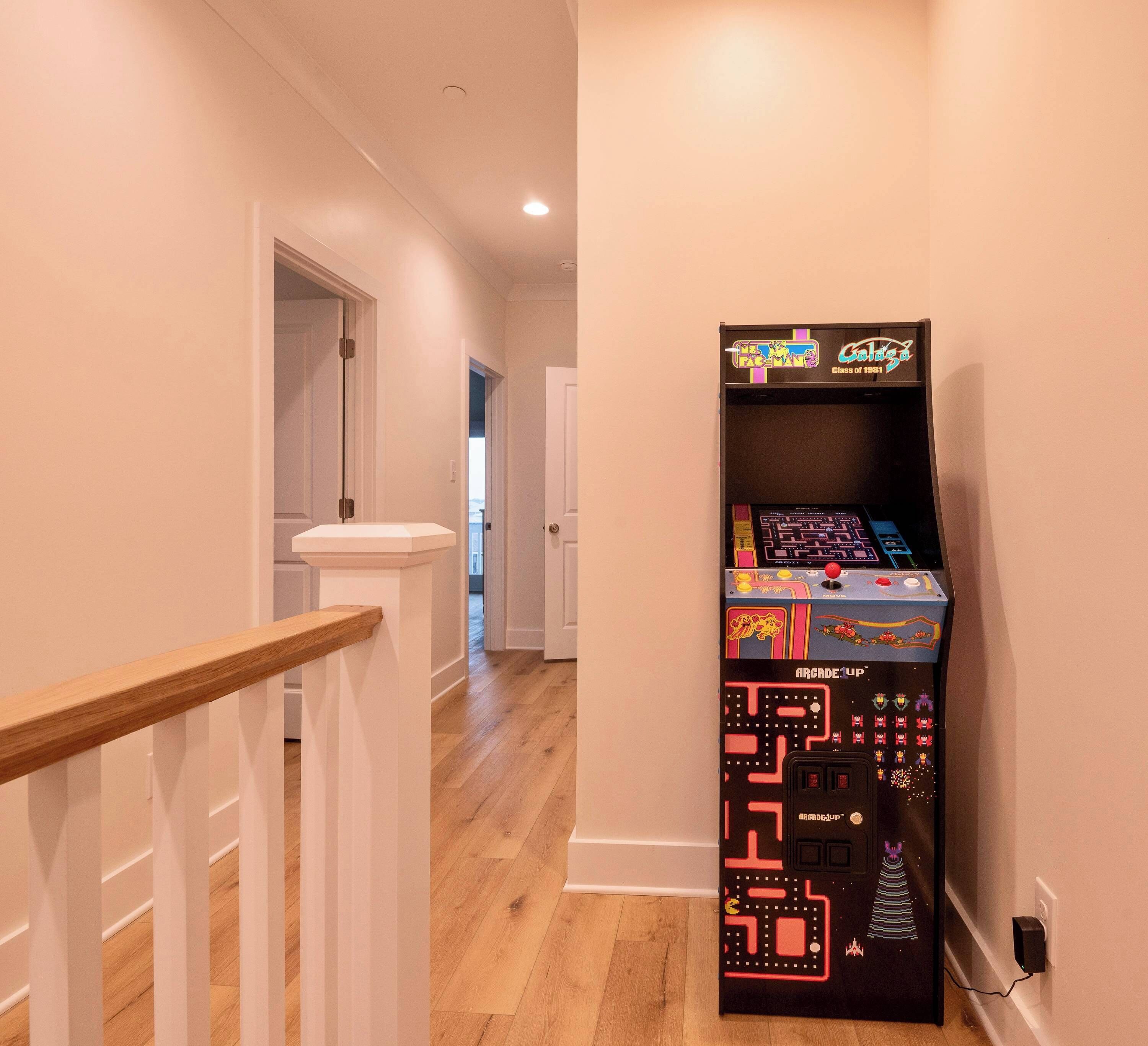 Corredor com escada de madeira e uma máquina de jogos eletrônicos retrô com a inscrição 'Arcade Uplift' na parede.