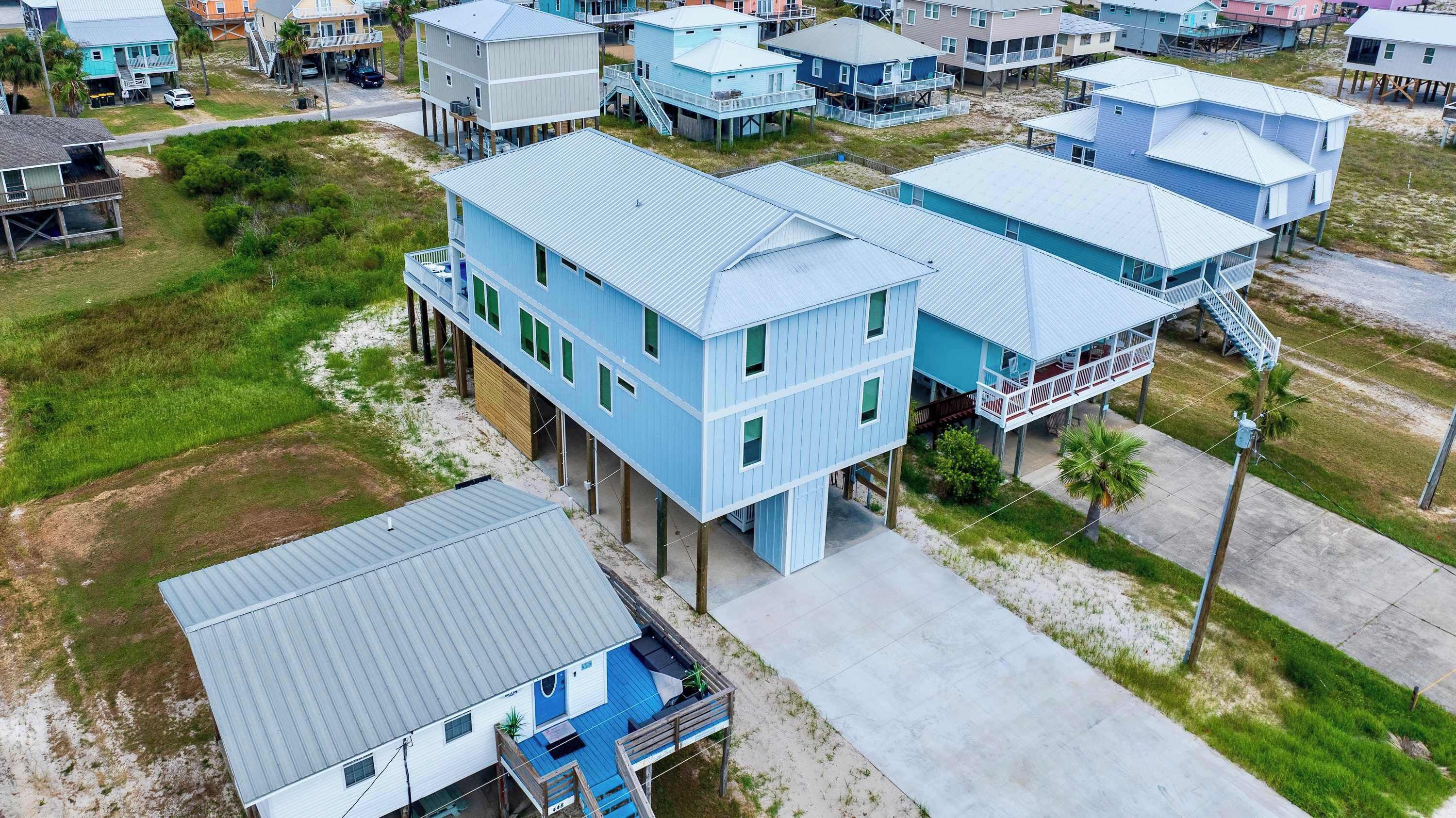 A coastal residential area with multiple two-story houses elevated on stilts, featuring balconies and a sandy beach in the background.