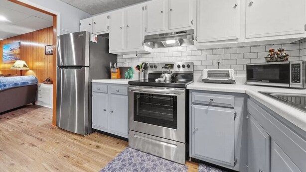 Una cocina moderna con electrodomésticos de acero inoxidable, armarios blancos y piso de madera.