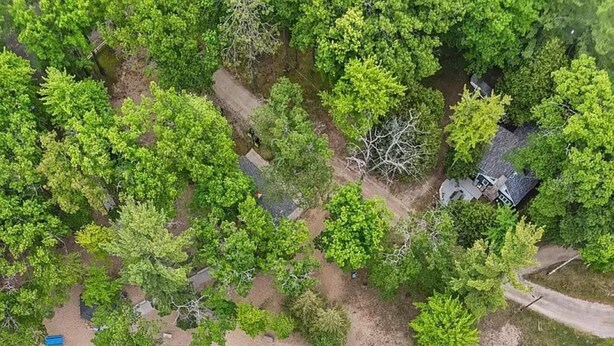 Ett flygbildsbild av en fastighet vid kusten med en sandstrand, tät vegetation och ett litet hus.