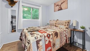 Un dormitorio con una cama grande, una ventana con vistas a la vegetación, una cabeza de animal montada en la pared y un estante fijado a la pared.