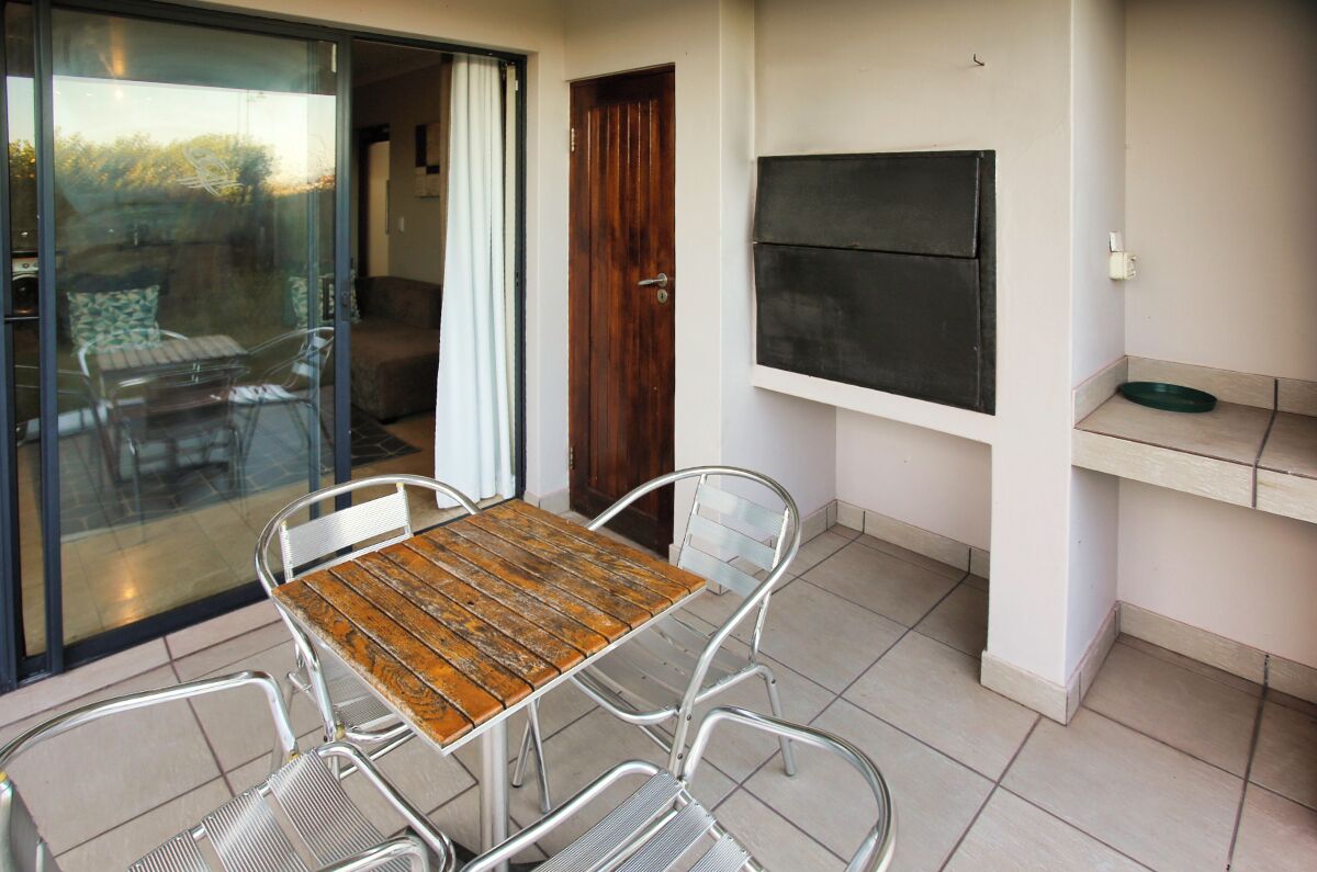 Uma sala de jantar com mesa de madeira e cadeiras de metal, uma porta de vidro deslizante, uma porta de madeira e uma TV preta fixada na parede.