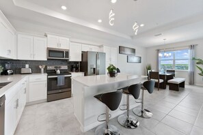 Una cocina moderna con armarios blancos, electrodomésticos de acero inoxidable y una isla central con taburetes.