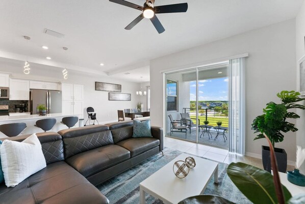 A modern living room with a leather sofa, a coffee table, and a view of the outdoors through large sliding glass doors.